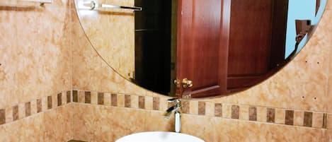 Un baño con un espejo redondo, un lavamanos blanco y un dispensador de toallas.