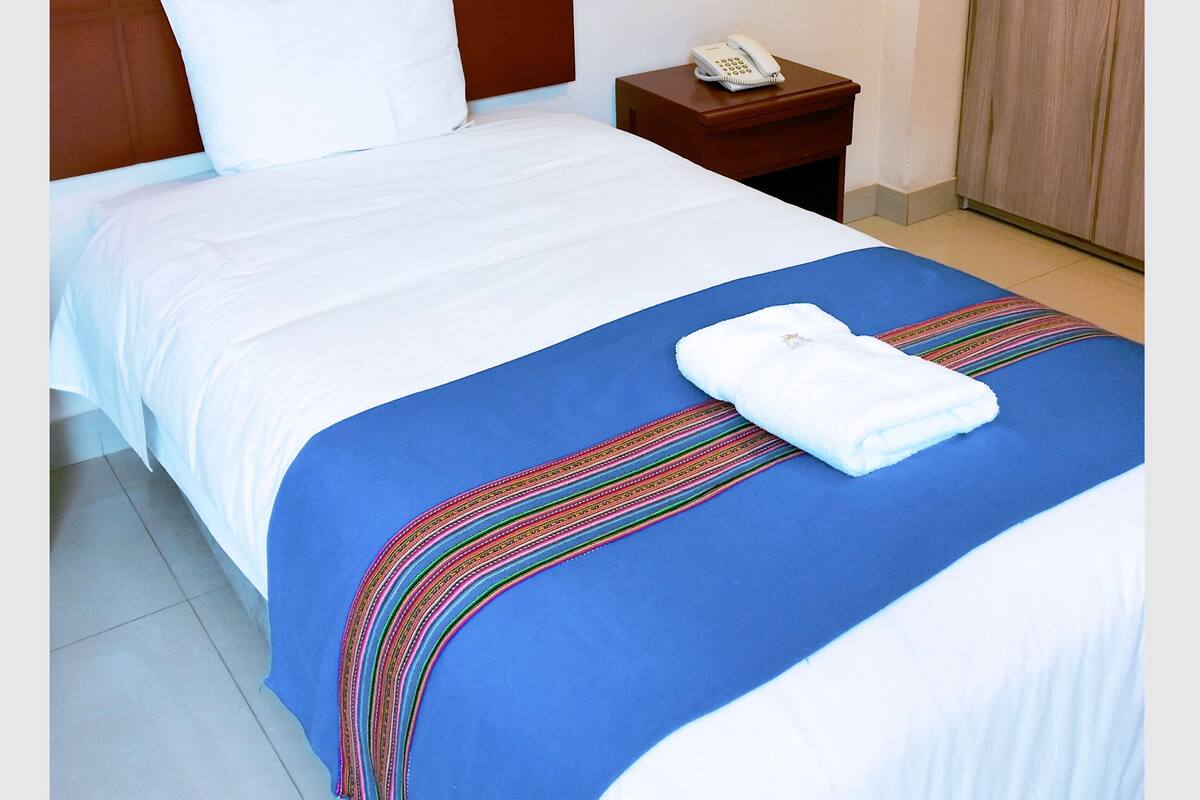 Ein Hotelzimmer mit einem Bett, einem Nachttisch mit Telefon und einem Holzschrank.