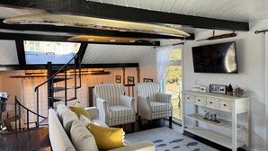 Un salon moderne avec un escalier, des fauteuils à rayures, un canapé et un téléviseur fixé au mur.