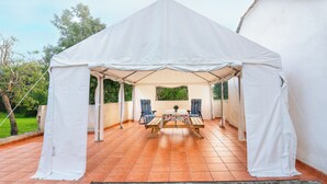 Una carpa blanca con una mesa y sillas en el centro, rodeada por un patio con baldosas.