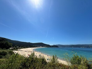 A beach with clear blue water, sandy shore, and green hills in the background.