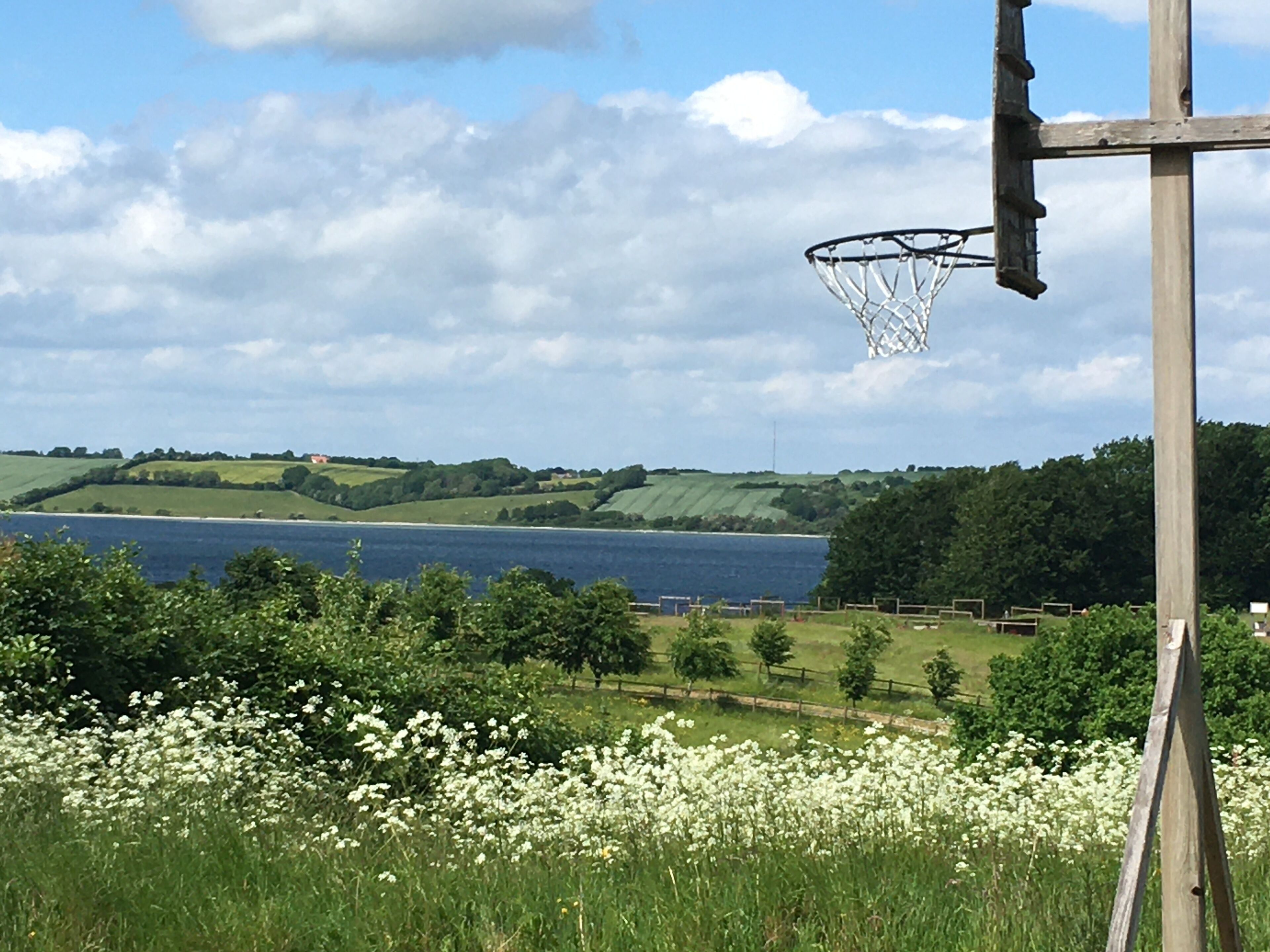 Un aro de baloncesto en un campo con un lago y colinas al fondo.