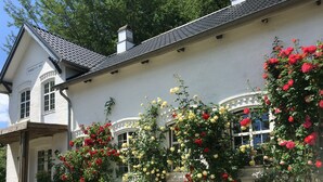 A white building with a tiled roof, a chimney, and a sign reading "BAKKE LY 1911". There are white chairs and a table in front of the building, surrounded by a gravel area. - Ferienwohnung 6 (Broager)