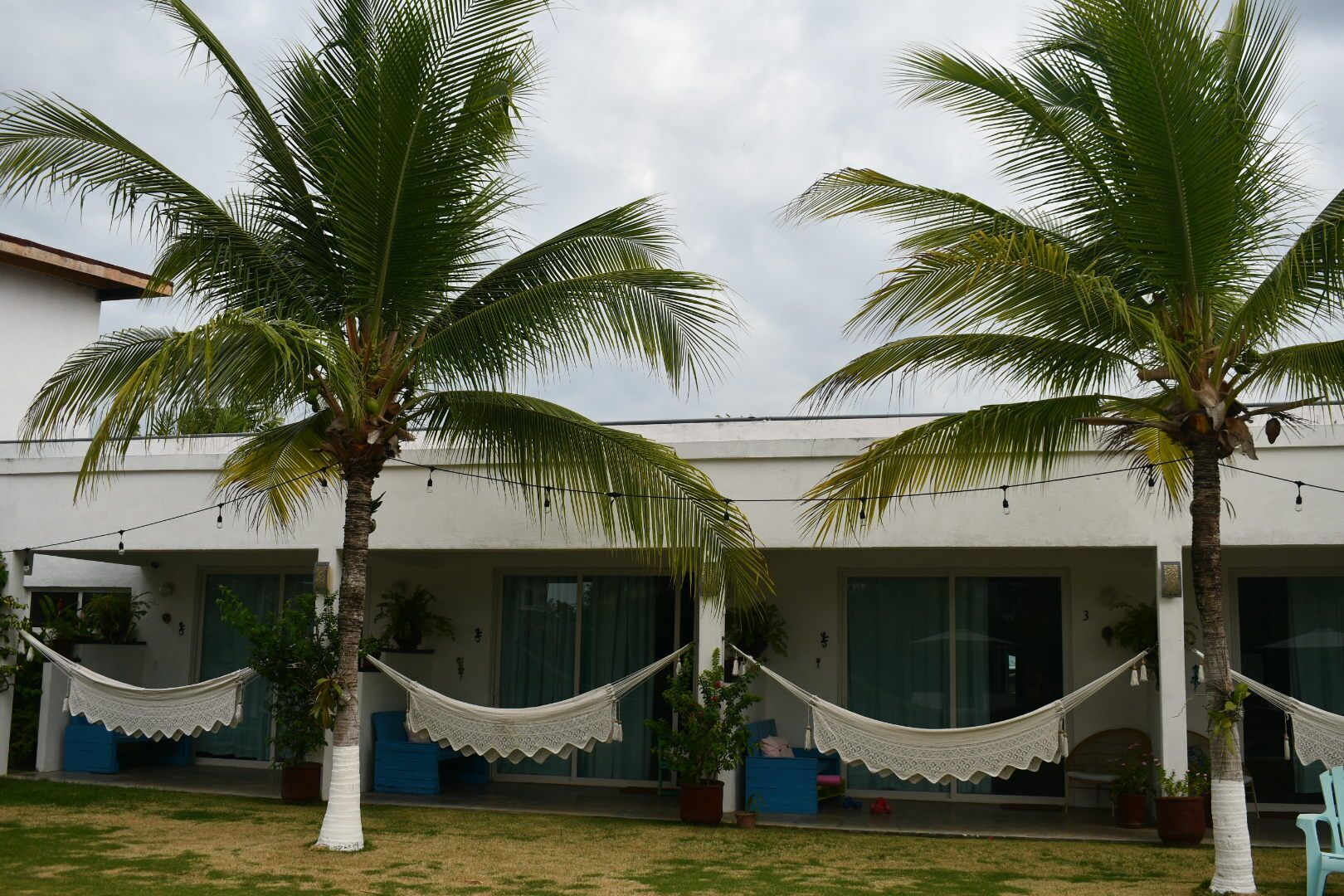 Un edificio con dos palmeras en primer plano, una hamaca y una silla azul.
