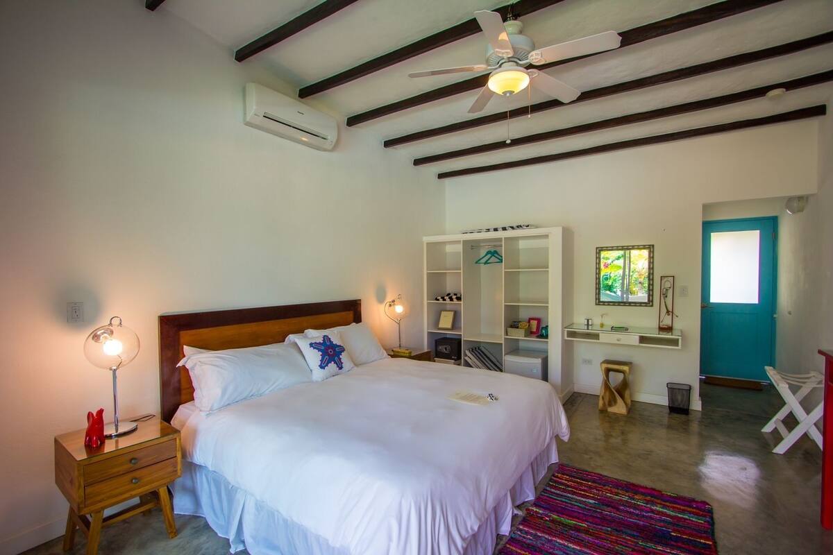 Un dormitorio con cama, mesitas de noche, armario, espejo y ventilador de techo.