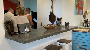 A kitchen with a bar area, stools, a fan, and a decorative wall piece. - Arganama (San Jose)