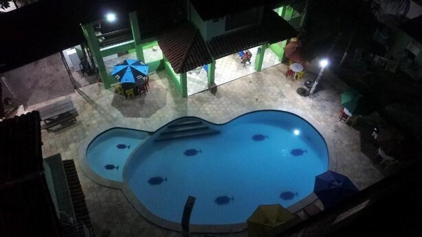 Piscina con múltiples carriles y una piscina infantil, rodeada por una zona cubierta con asientos y sombrillas.