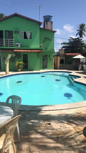 A swimming pool with a green house in the background. - Pousada Samburá (Ipojuca)