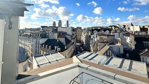 Eine Dachterrasse mit freiem Blick auf eine Stadtlandschaft, die moderne und traditionelle Gebäude unter blauem Himmel mit vereinzelten Wolken zeigt.