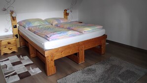 A single bed with a wooden frame, a nightstand, a dresser, and a patterned rug in a room with white walls and a sloped ceiling.