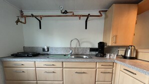 A compact kitchen with a sink, a coffee maker, and a kettle on the counter.