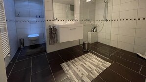 A modern bathroom with a toilet, sink, mirror, and shower.