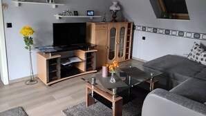 A living room with a flat-screen TV, wooden cabinets, a glass coffee table, and a sofa.