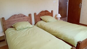 Una habitación con dos camas de madera, ropa de cama verde, una lámpara de noche y un armario de madera.