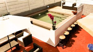 Un espace piscine comprenant un jacuzzi, des sièges et un bar avec des tabourets.