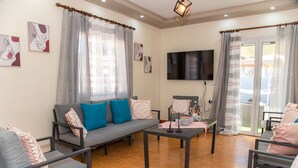 Un salon moderne avec un canapé gris, des coussins bleus et roses, une table basse et un téléviseur à écran plat.