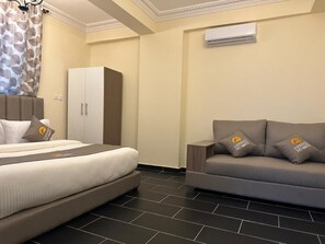 A hotel room with a bed, a sofa, a wardrobe, and an air conditioning unit. - Cereno Homes Accra (Accra)