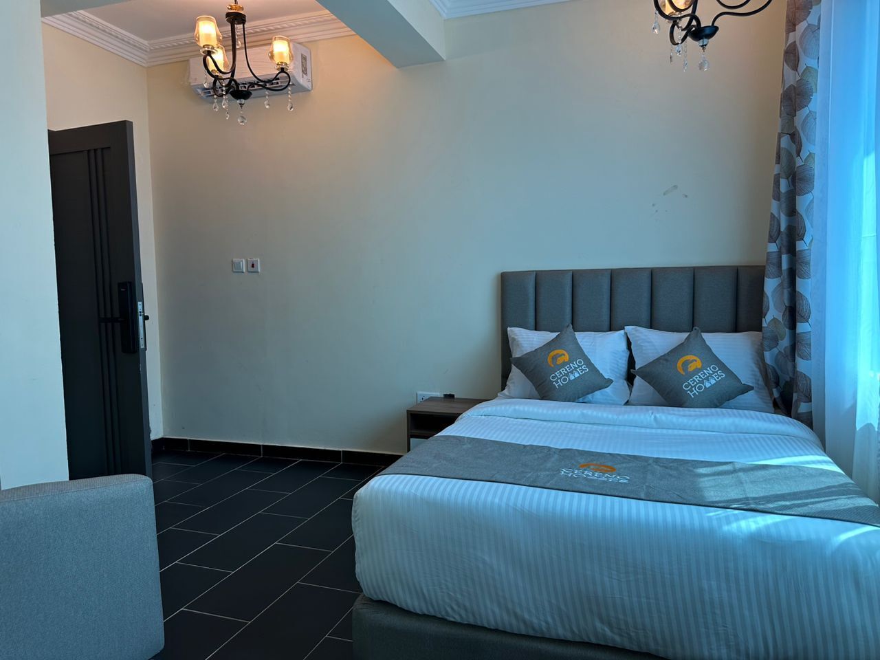 Una habitación de hotel con cama, mesita de noche, silla, candelabro y puerta.