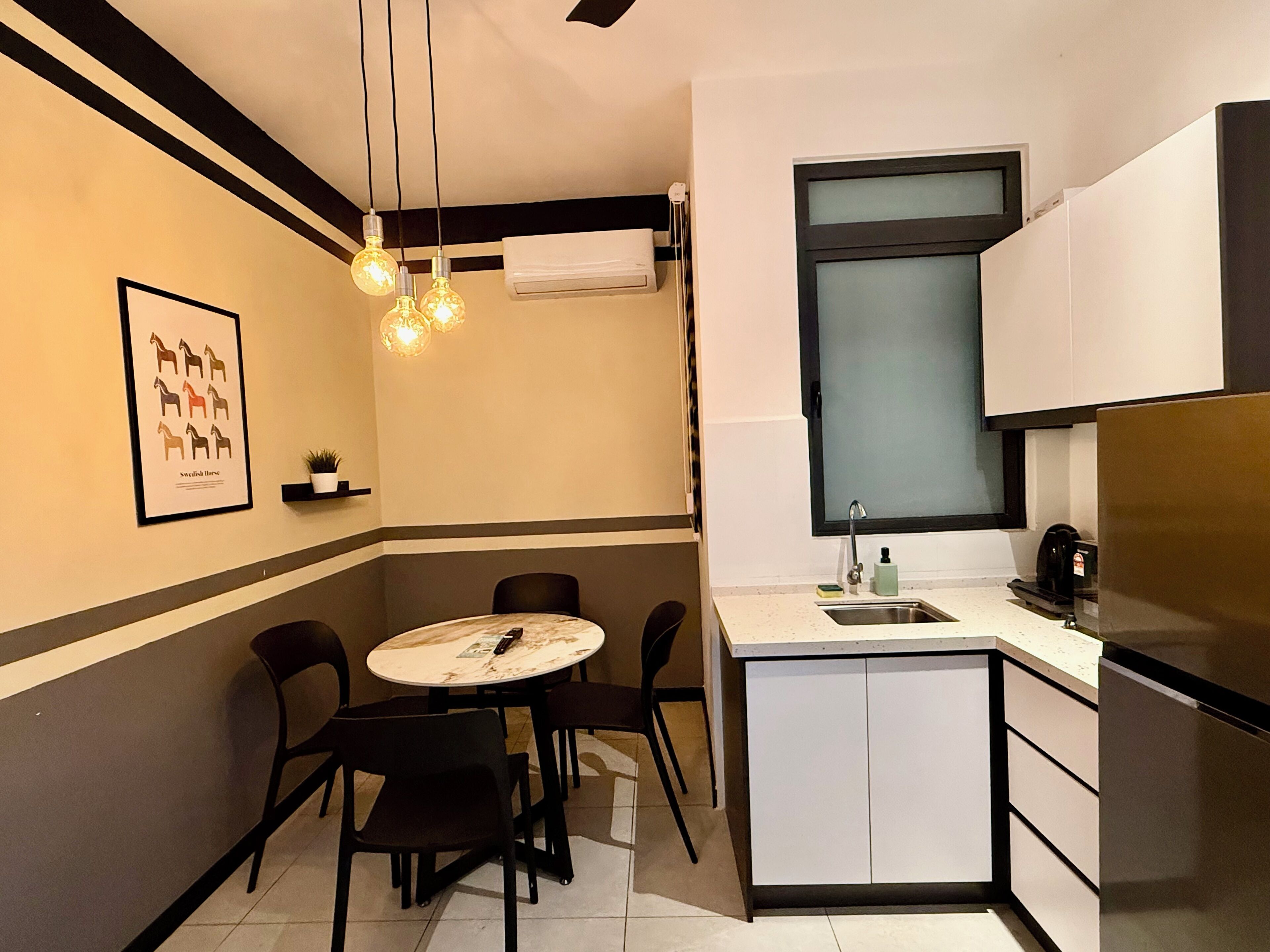 A compact kitchen with a dining area, featuring a round table, chairs, a refrigerator, and a window with a frosted glass panel.
