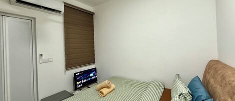 A bedroom with a bed, a television, an air conditioning unit, a ceiling fan, a window with blinds, and a door.