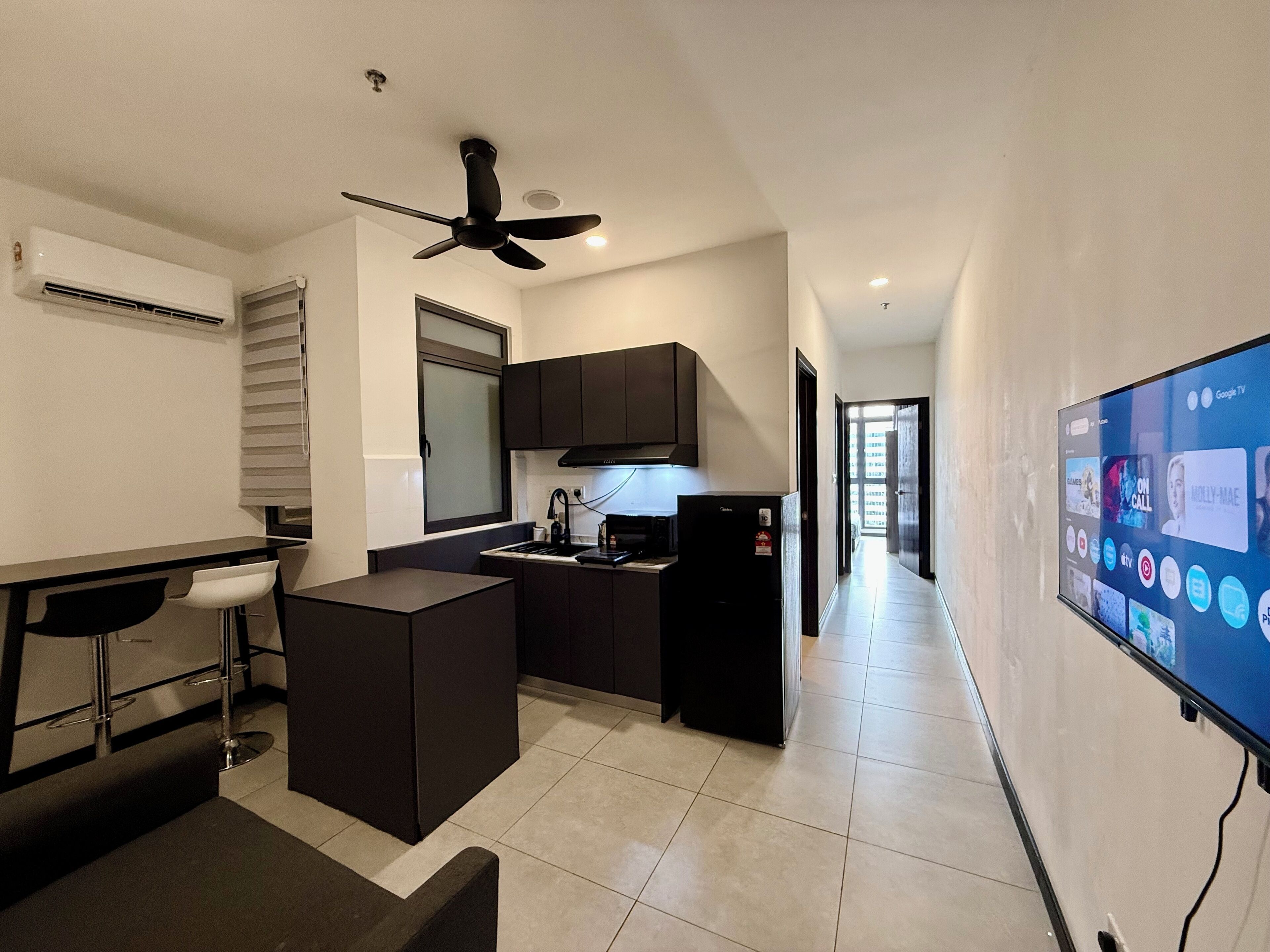 A compact kitchen with a central island, a ceiling fan, and a built-in TV displaying various channels.