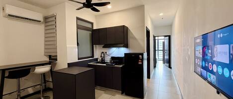 A compact kitchen with a central island, a ceiling fan, and a built-in TV displaying various channels.
