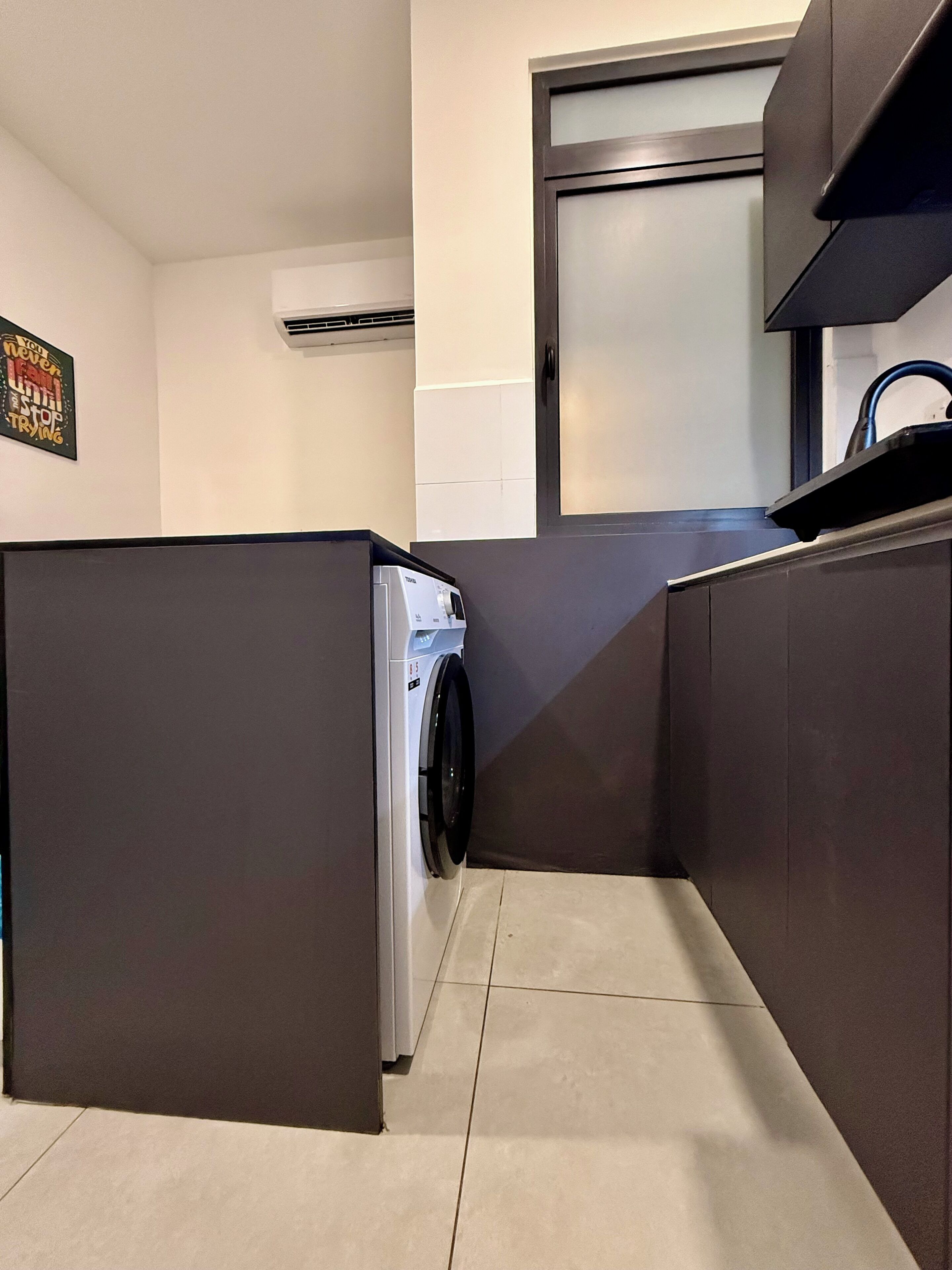 Cocina compacta con lavadora y secadora integradas, encimera oscura y un lavamanos pequeño.