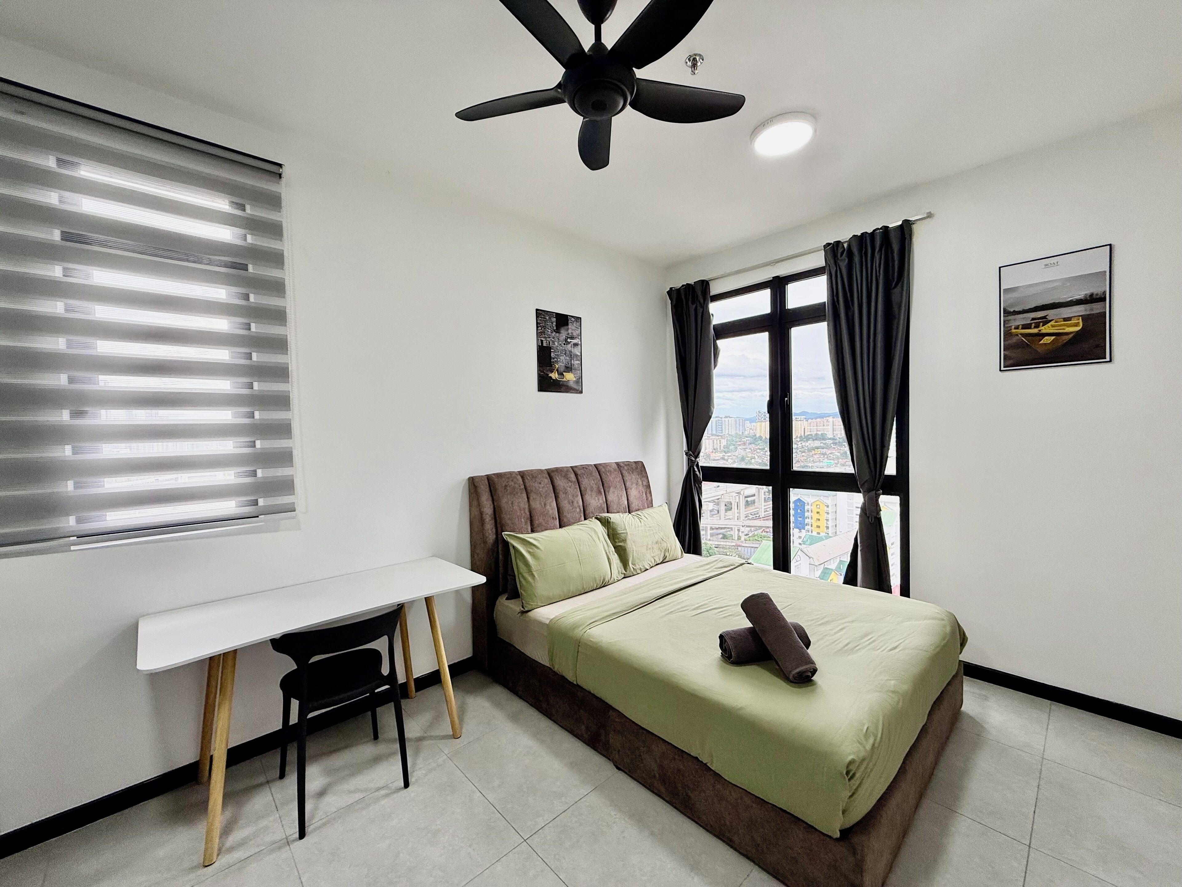A bedroom with a bed, a desk, a chair, a ceiling fan, a window with curtains, and two wall-mounted pictures.