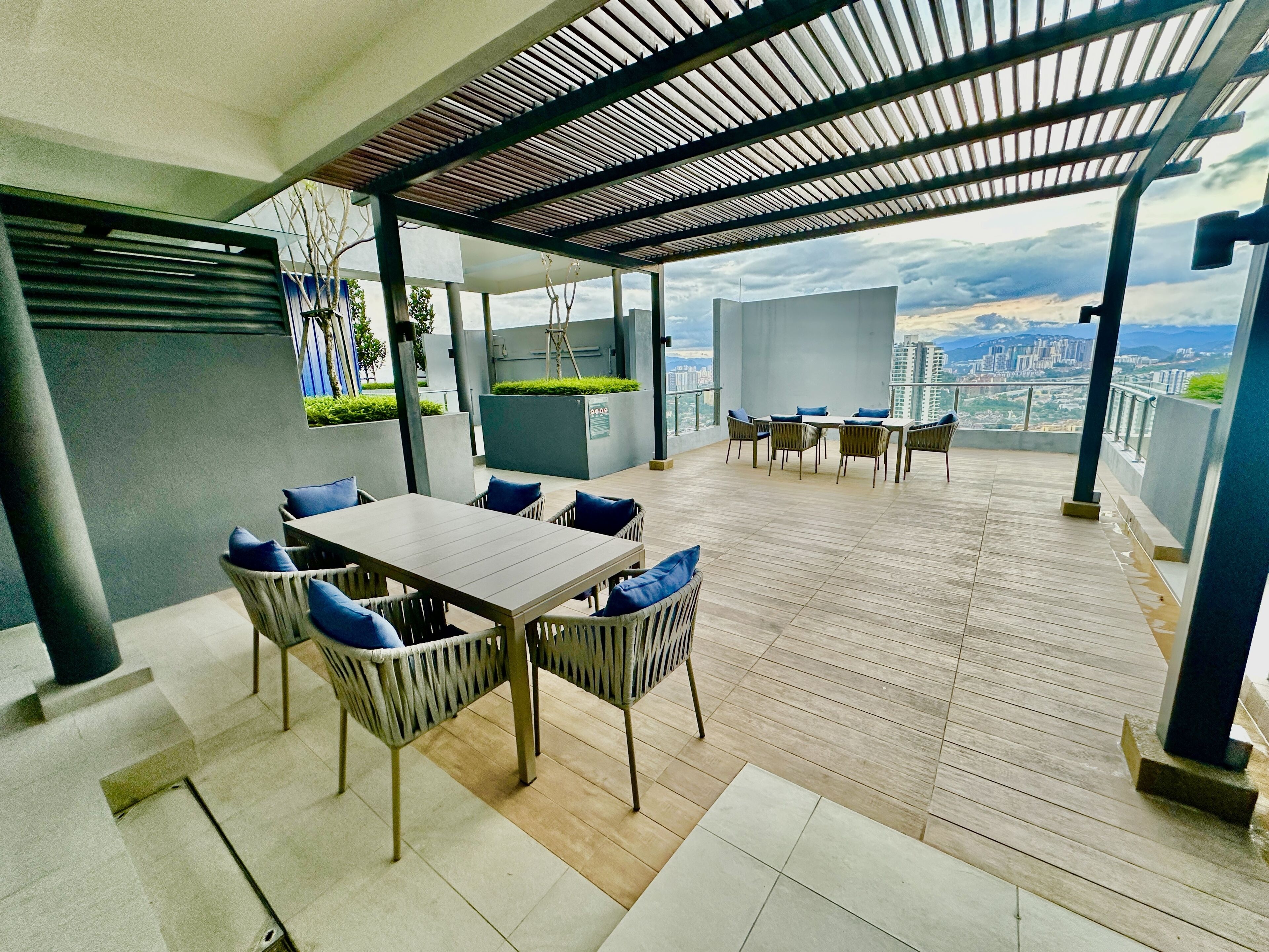 Une terrasse extérieure moderne, dotée d’un plancher en bois, d’une table à manger avec des chaises et offrant une vue sur le paysage urbain.