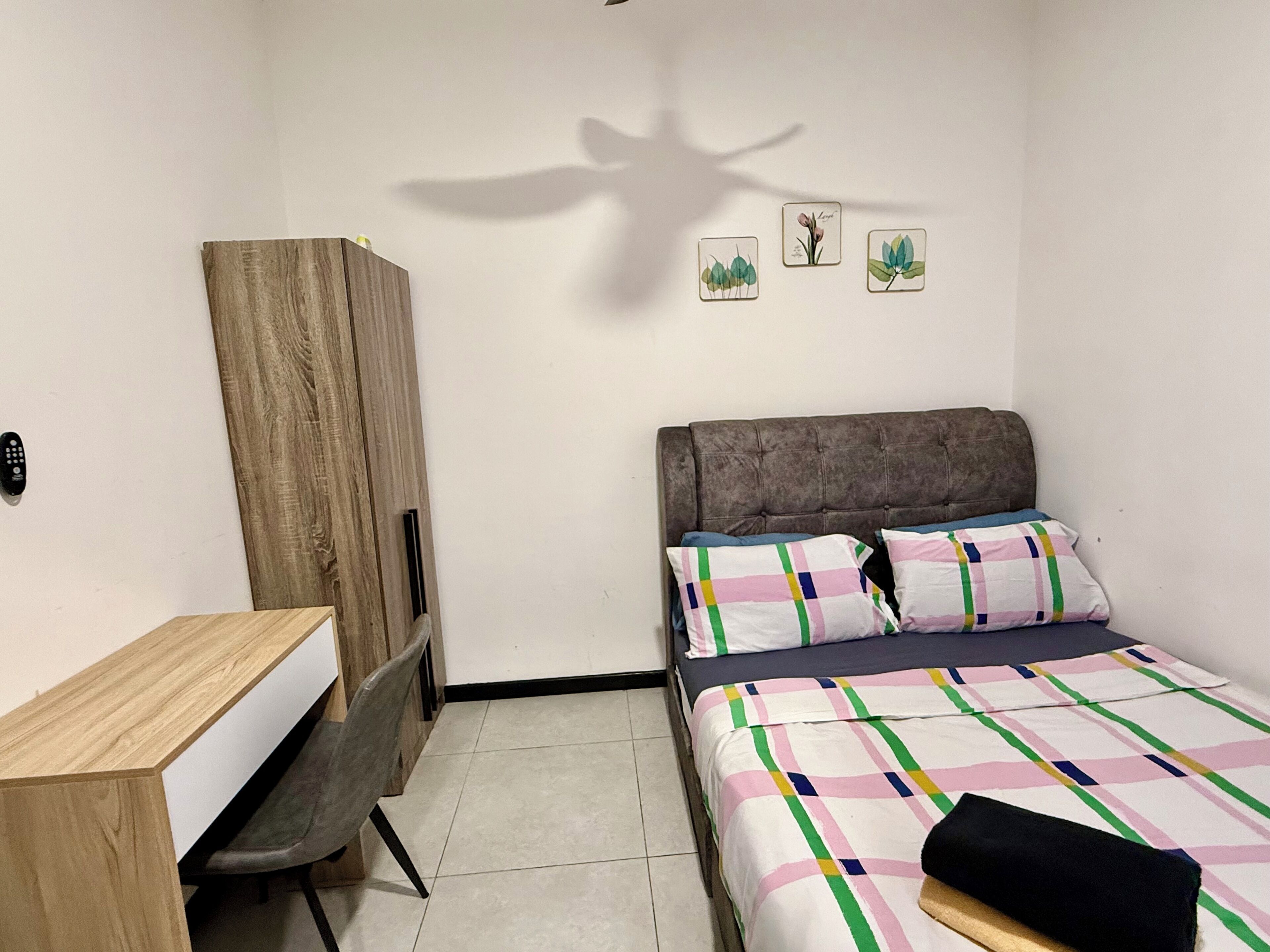 A bedroom with a bed, a desk, a chair, a wardrobe, and a ceiling fan.