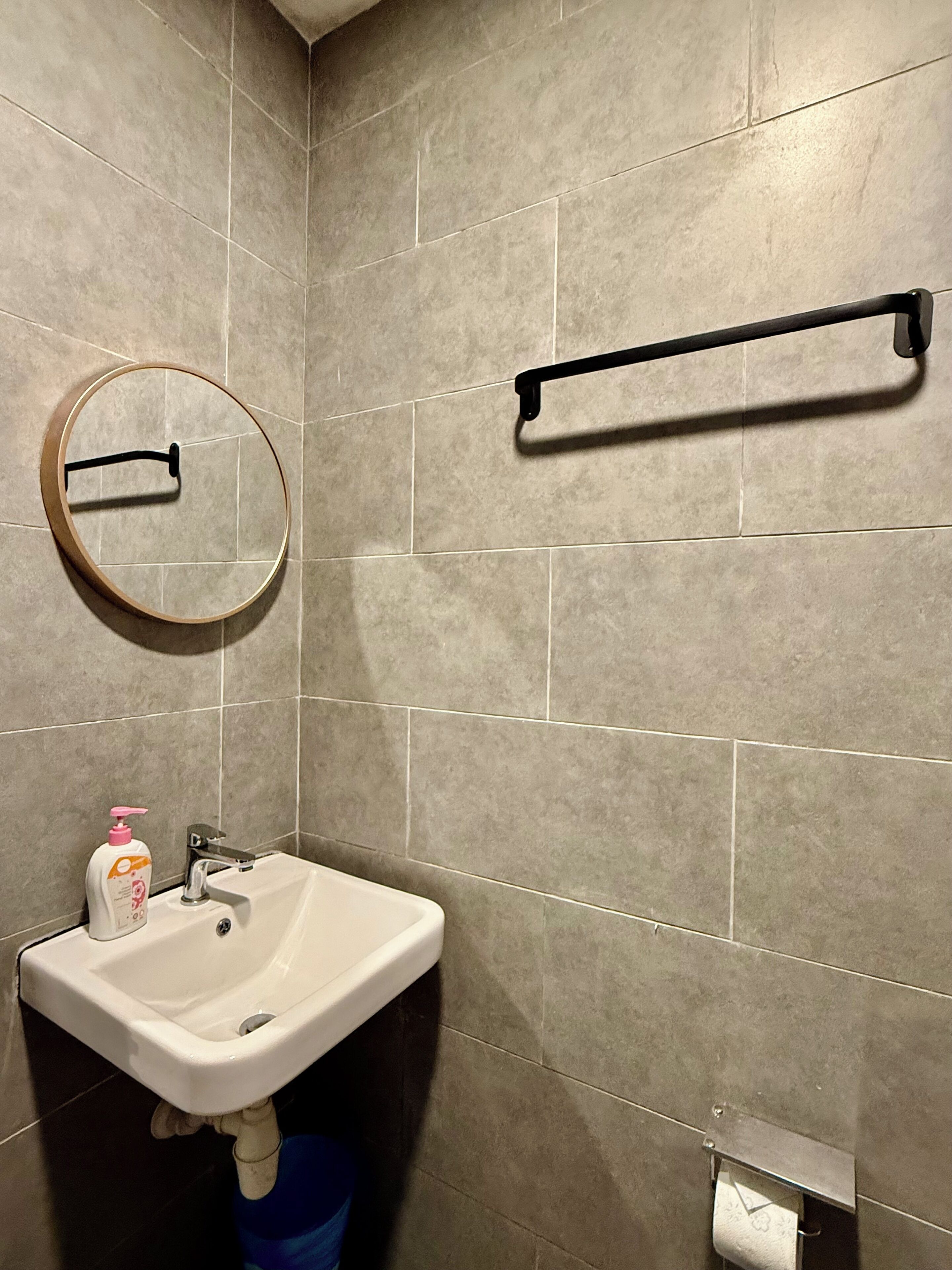 A bathroom with a sink, mirror, towel rack, and toilet paper holder.