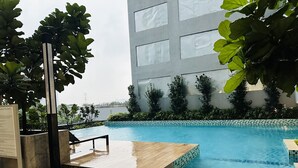 A swimming pool with a wooden deck, surrounded by greenery and a modern building in the background. - Neu Suites by Moonlight  (Kuala Lumpur)