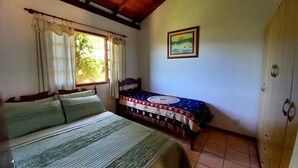 A bedroom with a bed, a smaller bed, a wardrobe, a window with curtains, and a painting on the wall.