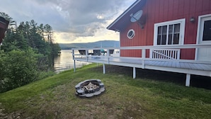 A red building with a deck overlooking a lake, surrounded by trees. - Cozy Lake Front home for Boating, fishing, winter sports, and gorgeous views,  (Errol)