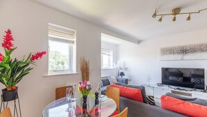 A modern living room with a glass dining table, grey sofas, and a flat-screen TV. - Skyline Haven Modern 2BR w/ Free Parking & 4kTV (London)