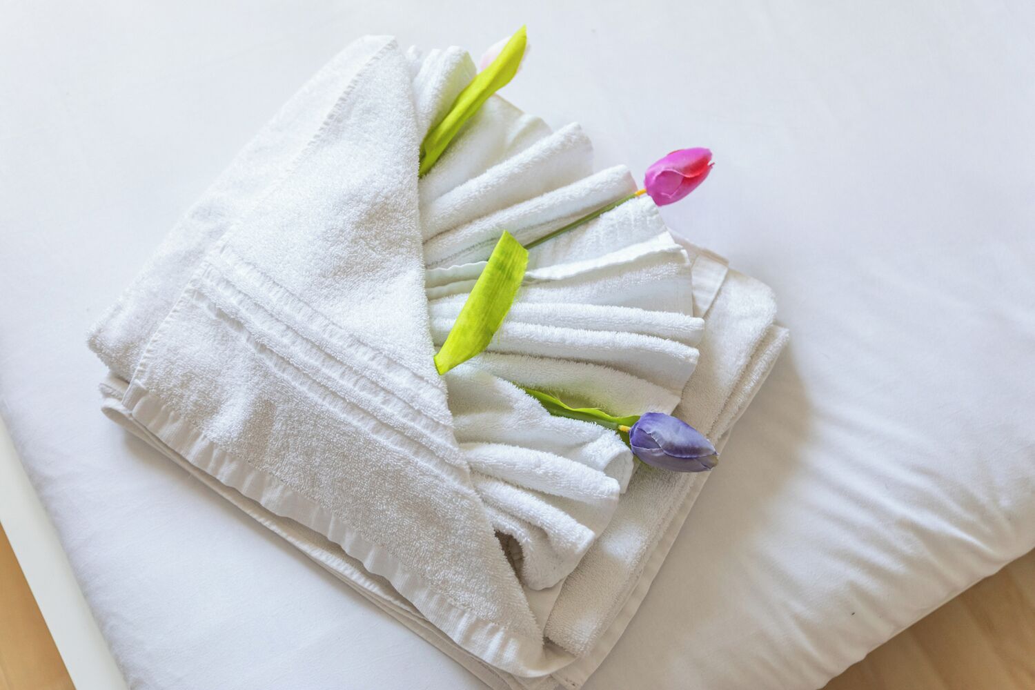A neatly folded white towel with green and purple flowers placed on a white pillow.