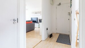 A hallway leading to a living area with a grey sofa, a television, and a small table. - Skyline Haven Modern 2BR w/ Free Parking & 4kTV (London)