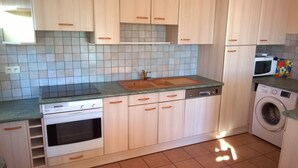 Uma cozinha com armários de madeira clara, uma pia dupla, uma lava-louças, um forno e uma máquina de lavar.