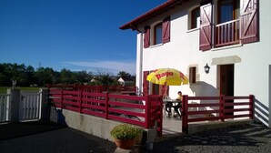 Um edifício com cerca de madeira vermelha, um guarda-sol amarelo e um vaso de planta.