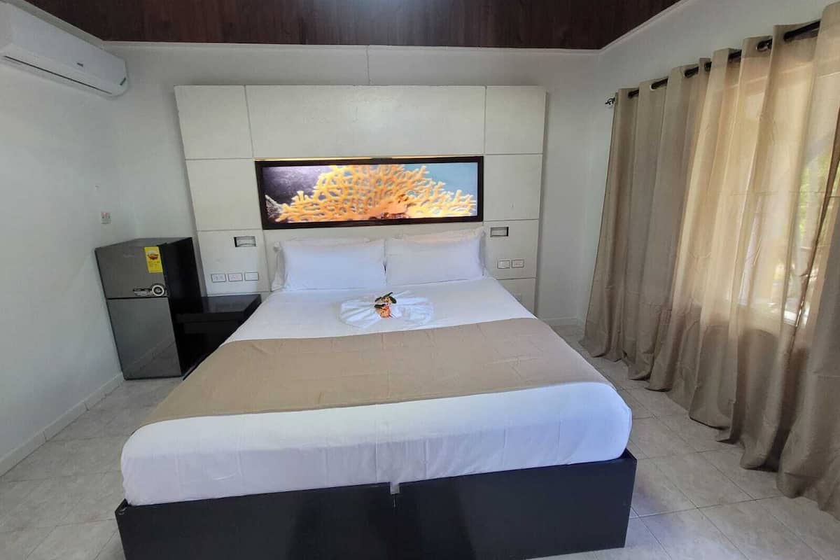Une chambre d’hôtel avec un lit, un téléviseur fixé au mur, un petit réfrigérateur et une fenêtre avec des rideaux.