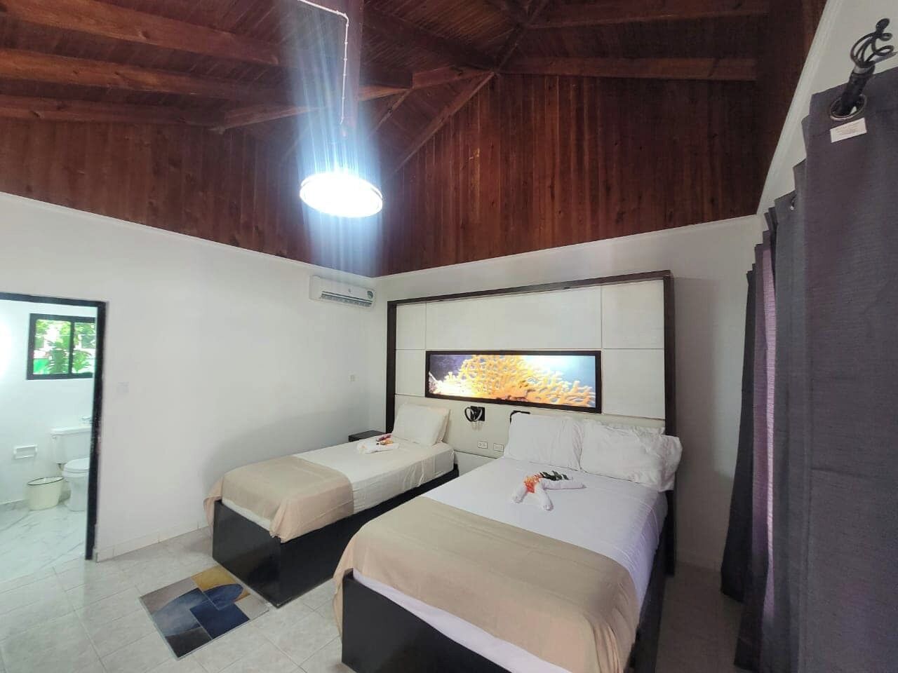Una habitación con dos camas, un televisor montado en la pared y techo de madera.