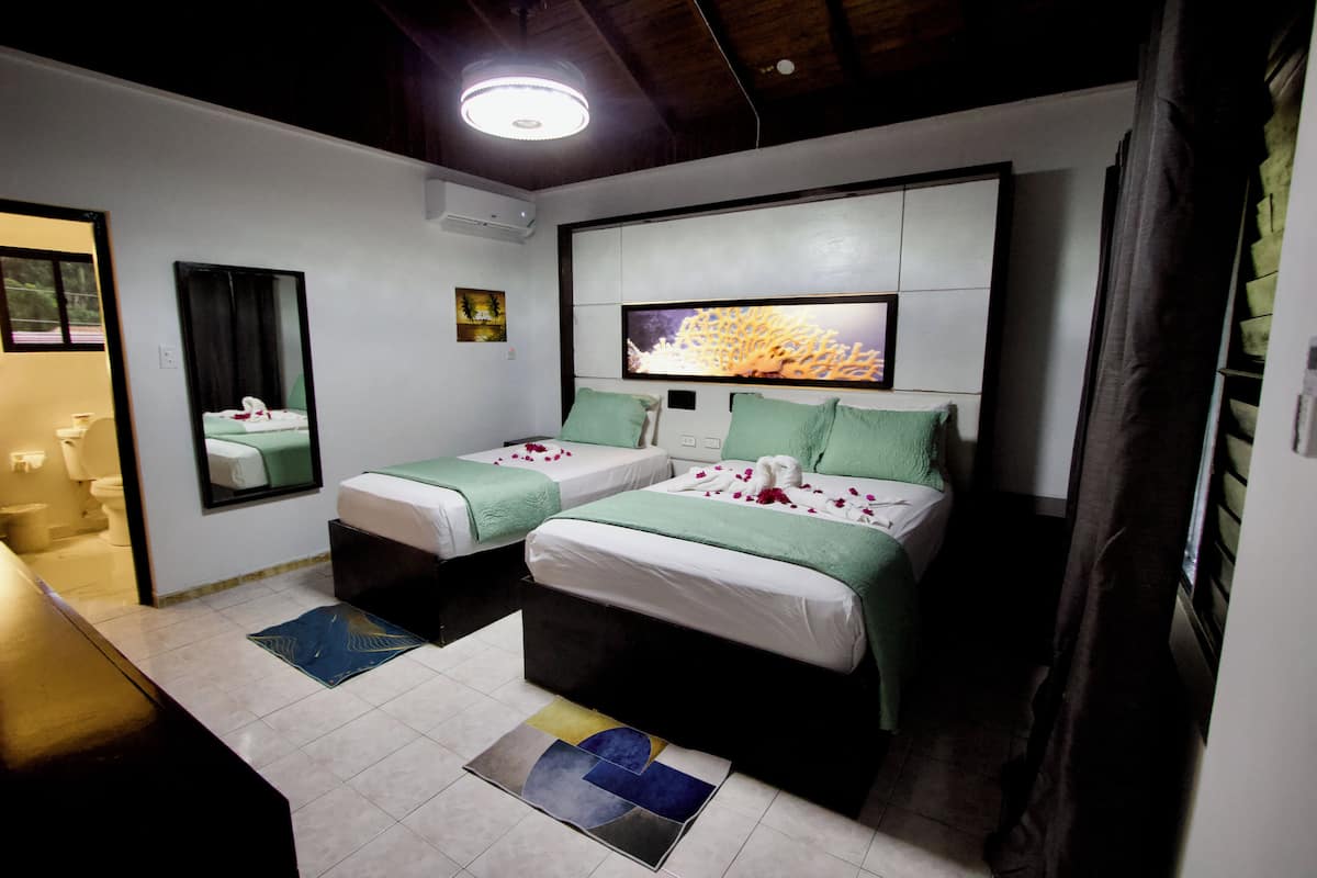 Une chambre d’hôtel avec deux lits, un grand tableau au mur, un miroir et une salle de bain visible à travers une porte ouverte.