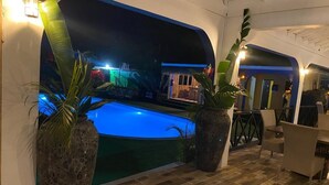 Un espace piscine offrant une vue sur un complexe hôtelier, agrémenté de plantes en pot et doté de sièges confortables.