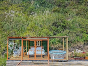 A glass-enclosed room with a bed, a hanging chair, and a mosaic hot tub.