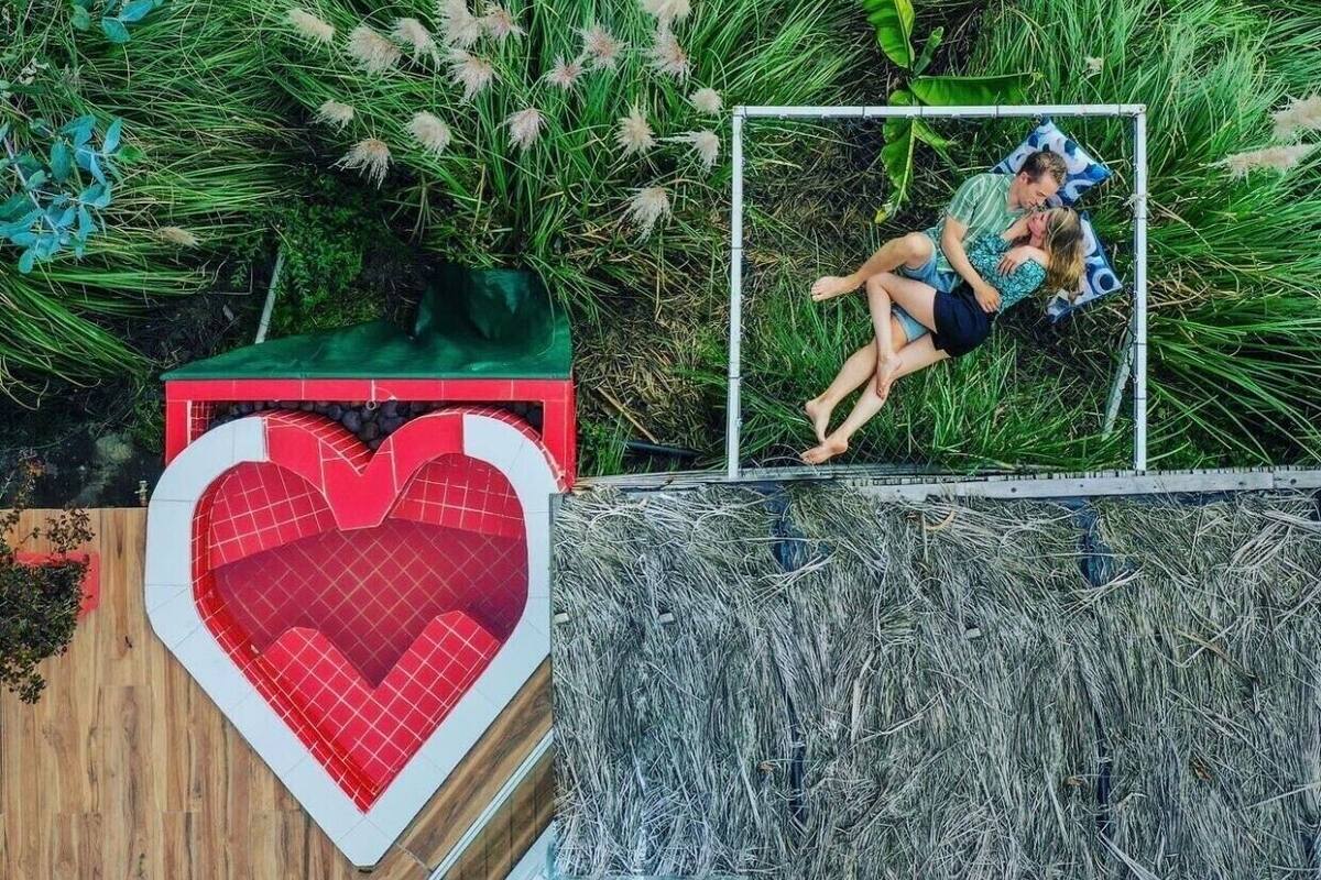 A heart-shaped pool with a red and white checkered pattern, surrounded by lush greenery and tall grasses.