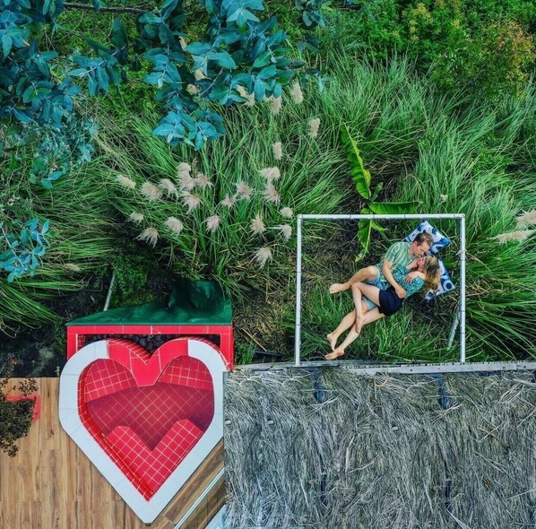 A heart-shaped pool with a red and white checkered pattern, surrounded by lush greenery and tall grasses. - Samay Collections (Tababela)