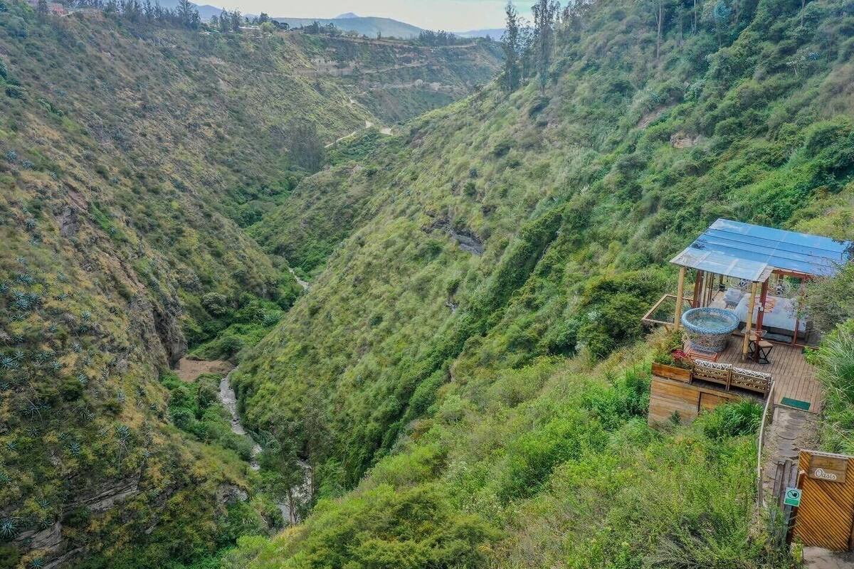 A hillside with a small wooden structure featuring a solar water heater and a seating area.