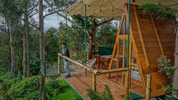 Uma cabana de madeira com uma ponte de corda, rodeada por árvores.