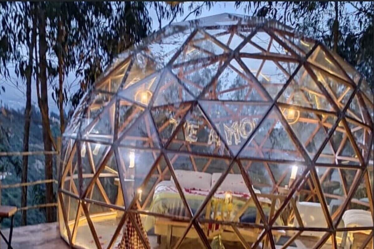 A geodesic dome structure with a bed inside, surrounded by a wooden deck and a pool.