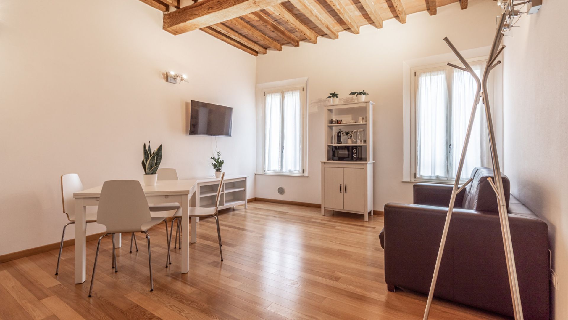 Un saló modern amb sostre de fusta, un televisor de pantalla plana penjat a la paret, una zona de menjador amb taula i cadires, i un sofà.